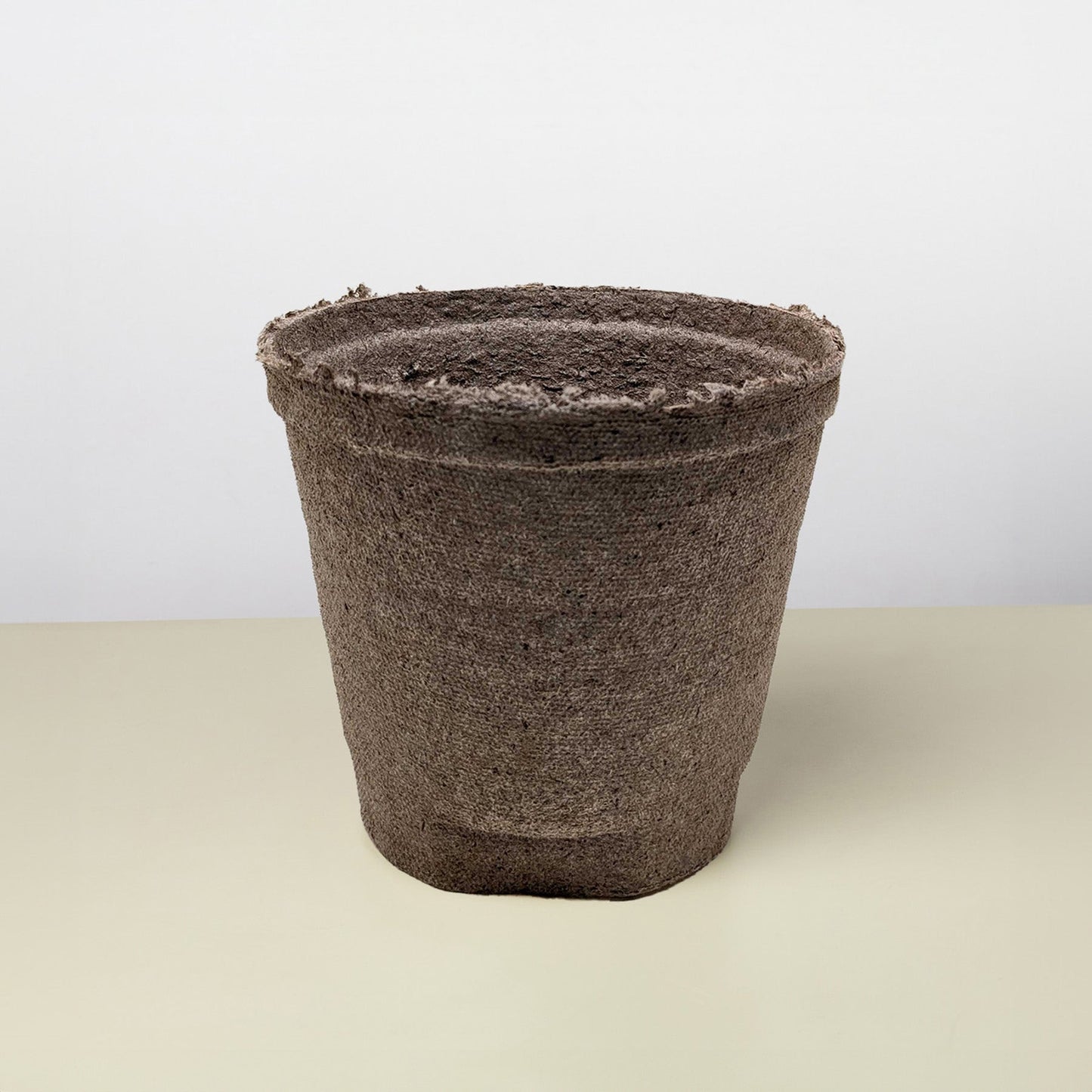 Empty, textured brown biodegradable plant pot with a rough rim on a light surface.