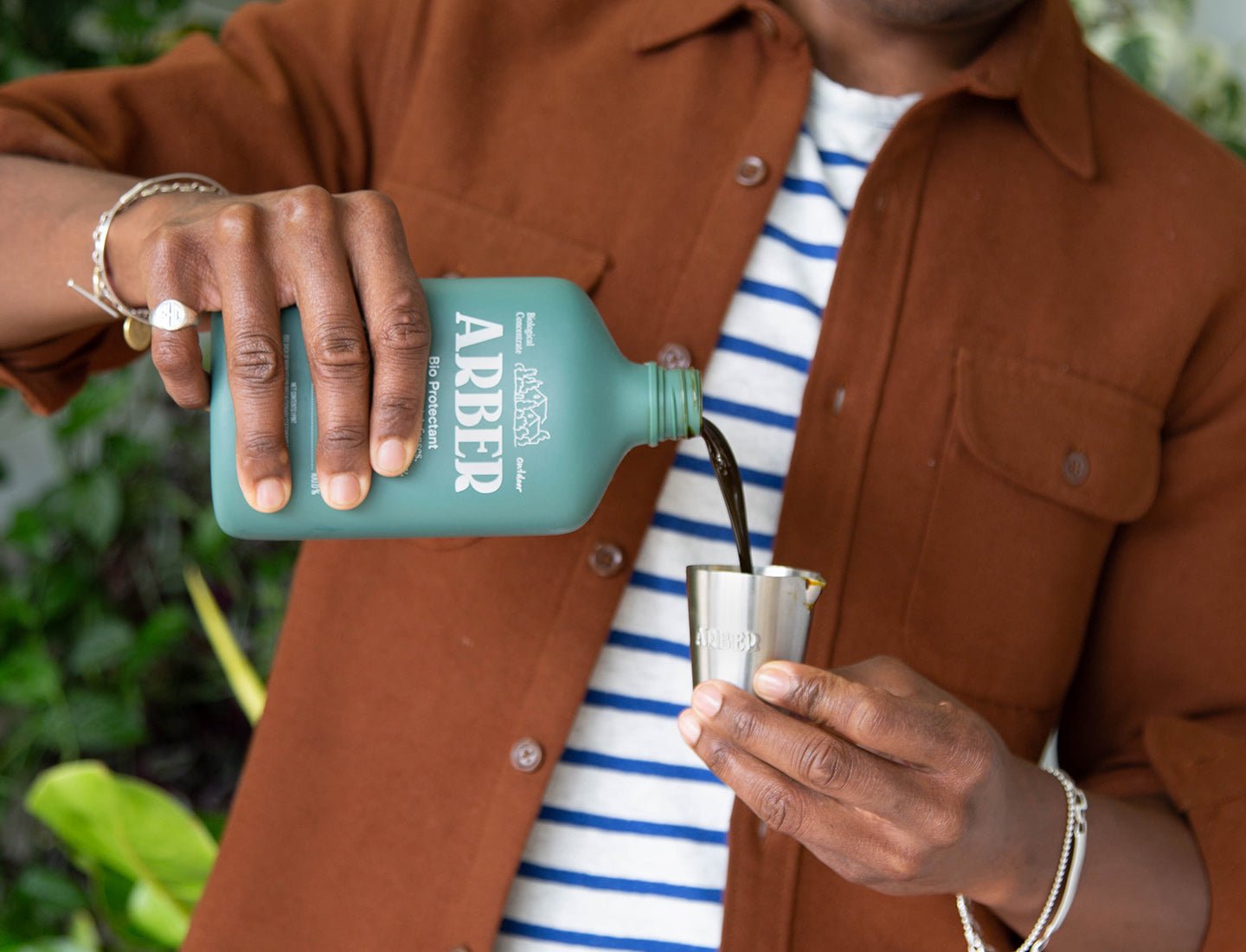 Man in a brown shirt pouring dark Organic Bio Protectant from a teal ARBER bottle into a silver jigger.