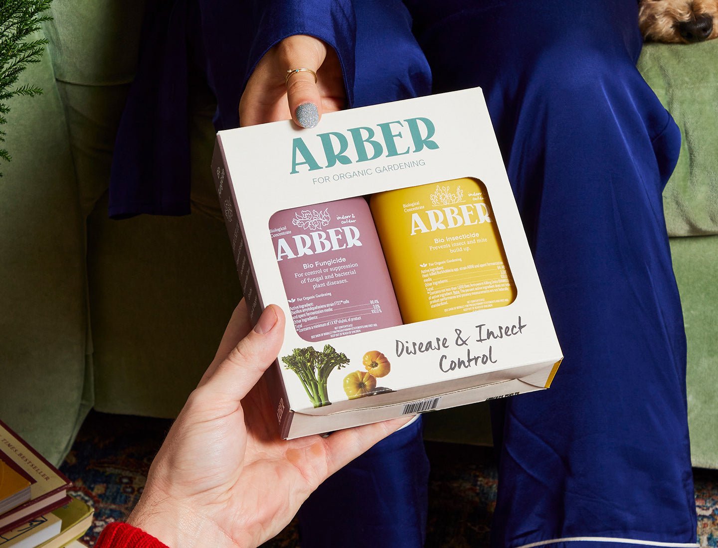 Hands holding an Arber Organic Disease & Insect Control Starter Set with green and yellow bottles in a white box.