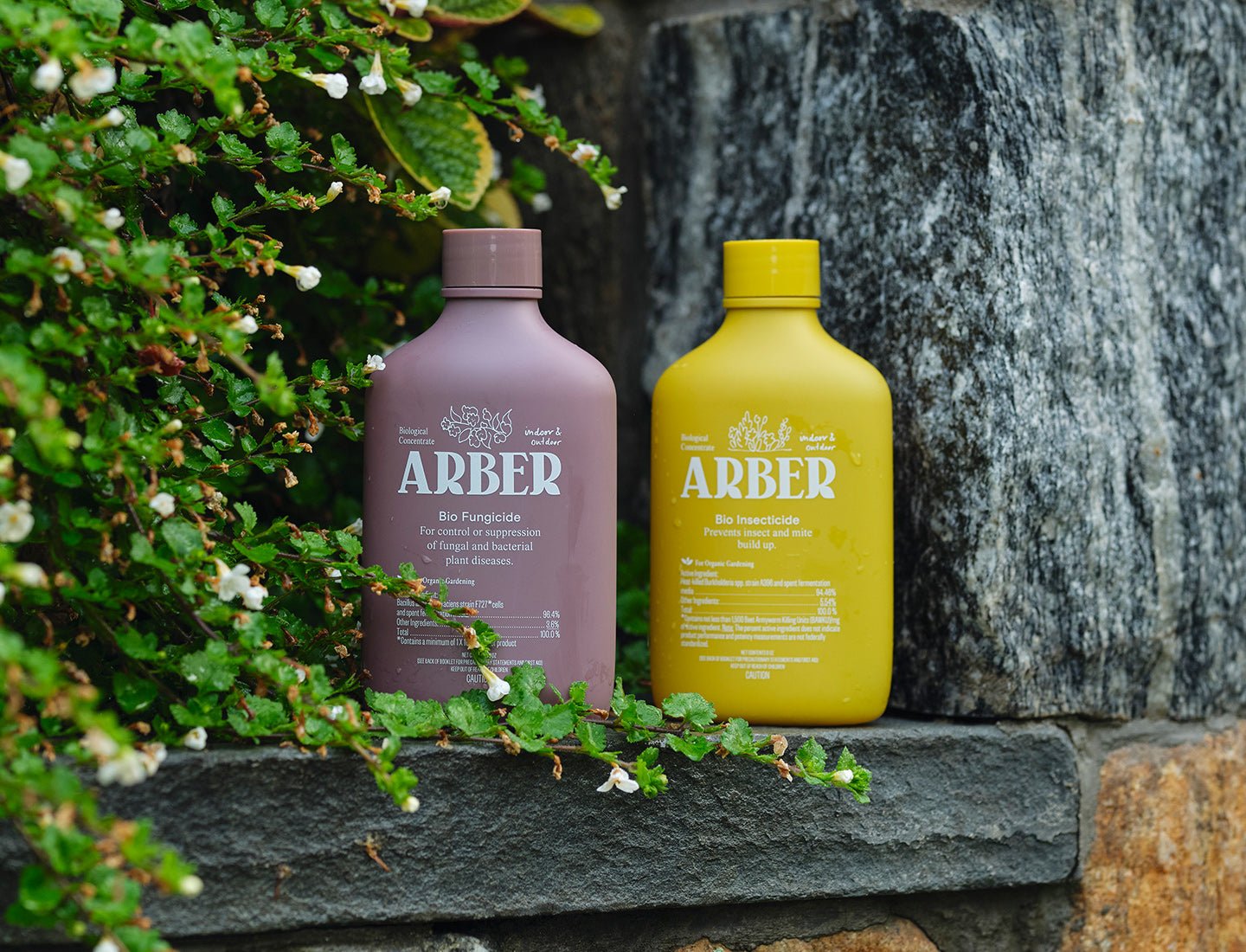 Two 8oz Arber bottles: a lavender Bio Fungicide and a yellow Bio Insecticide, on a stone ledge.