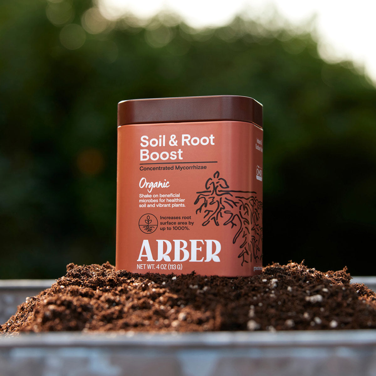 Brown ARBER Organic Soil & Root Boost container with white text, 4 oz, on a mound of dark soil.